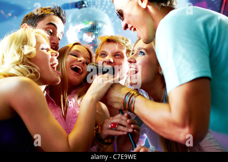 Portrait of joyous guys and girls singing at party in one microphone Stock Photo