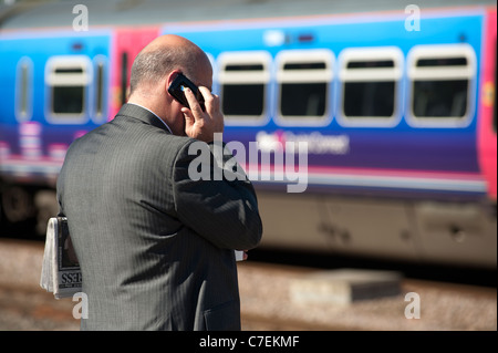 Businessman using a mobile phone waiting on a railway station platform. Stock Photo