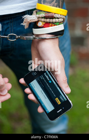 Handcuffed teenager holding an Apple iphone showing Twitter. Stock Photo