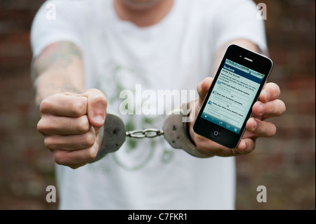 Handcuffed teenager holding an Apple iphone showing Facebook. Stock Photo