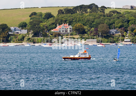 A pilot boat going up the River Fal opposite Falmouth, passing expensive properties at Flushing, Cornwall Stock Photo
