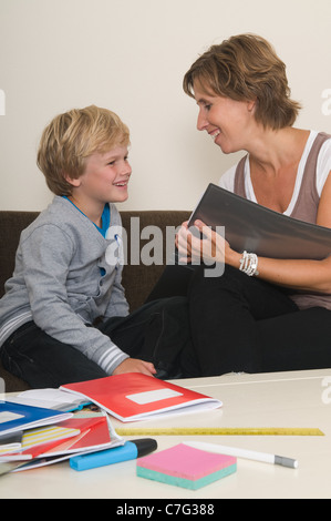 Boy is doing his homework in the livingroom while mother is helping him Stock Photo