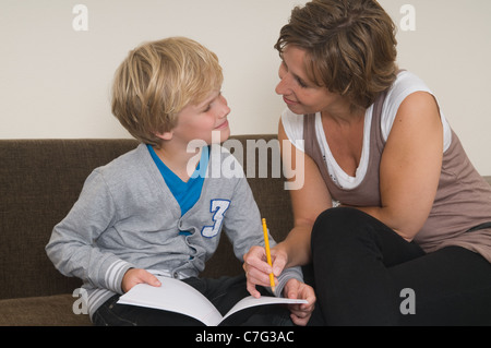 Boy is doing his homework in the livingroom while mother is helping him Stock Photo