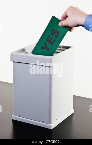 A man putting a ballot with the word YES written on it into a ballot box, close-up hands Stock Photo