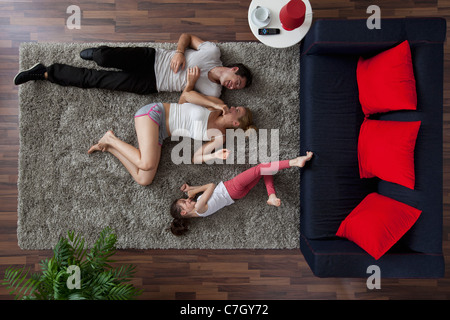 A family of three happily lying on a living room rug, overhead view Stock Photo