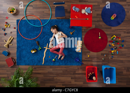 A little girl lying on a rug with toys, overhead view Stock Photo