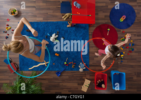 A mother and daughter using hula hoops in their living room, overhead view Stock Photo