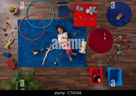 A little girl lying on a rug hugging stuffed animals, overhead view Stock Photo