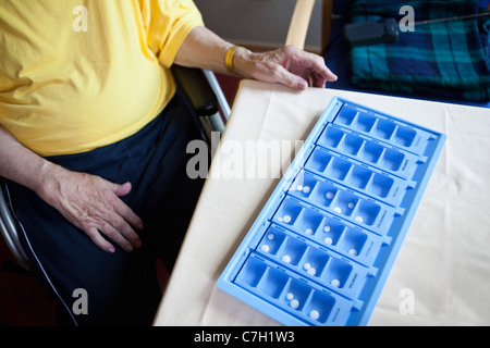 A senior man sitting next to a weekly pill organizer, focus on object Stock Photo