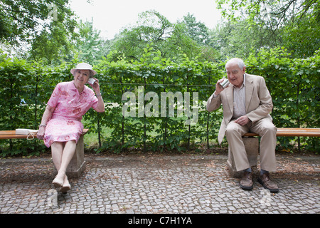 Senior man and woman speak to each other on tin can phones in park Stock Photo