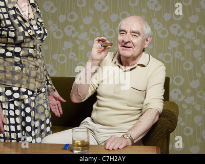 Senior man sitting on couch smoking cigar Stock Photo