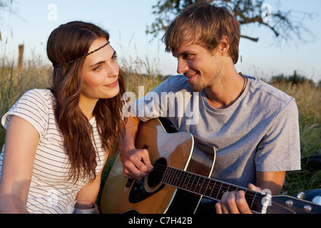 Man plays guitar to his girlfriend in field Stock Photo
