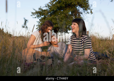 Three friends enjoying sitting in secluded field with wine and guitar Stock Photo