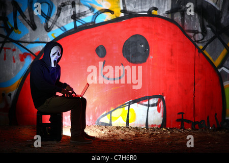 Computer user, hacker, sits conspiratorially with a laptop, in front of a graffiti. Symbol picture, computer-Internet crime. Stock Photo