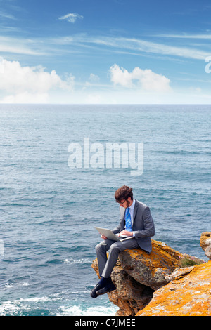 Businessman using laptop on cliff Stock Photo
