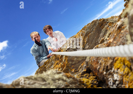 Businessmen pulling rope over cliff Stock Photo