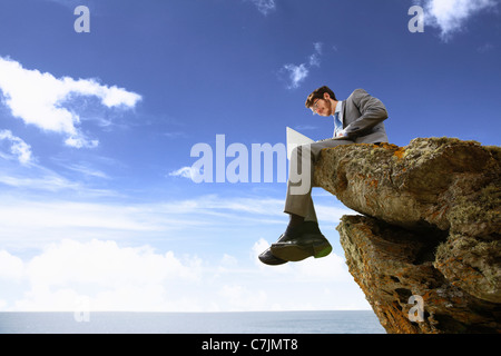 Businessman using laptop on cliff Stock Photo