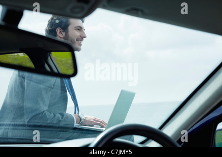 Businessman using laptop on hood of car Stock Photo