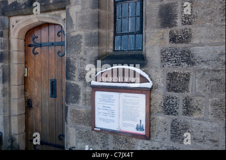 Church office exterior, wooden entrance door close-up (strap hinges) stone wall & snow on noticeboard - All Saints Parish Church, Ilkley, England, UK. Stock Photo
