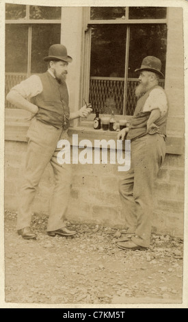 Victorian photograph of two men drinking bottles of beer, smoking pipes and talking to each other Stock Photo
