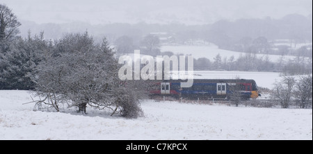 Snow falling on snowy winter day & local passenger railway train travelling past white rural fields - Wharfedale line, West Yorkshire, England, UK. Stock Photo