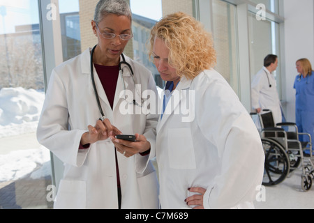 Two female doctors reading text message on a mobile phone with their colleagues standing in the background Stock Photo