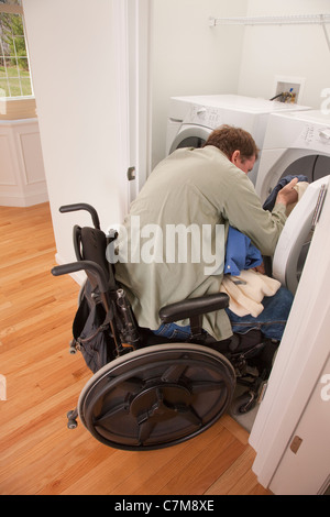 Man with spinal cord injury in a wheelchair doing his laundry at home Stock Photo