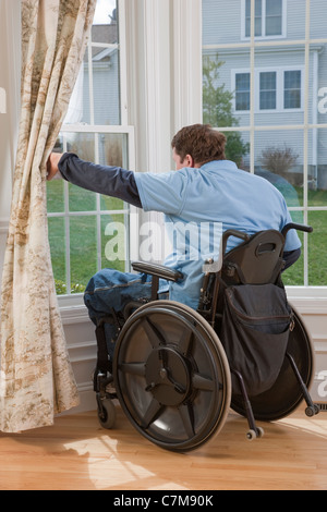 Man with spinal cord injury in a wheelchair looking out the window of his accessible home Stock Photo