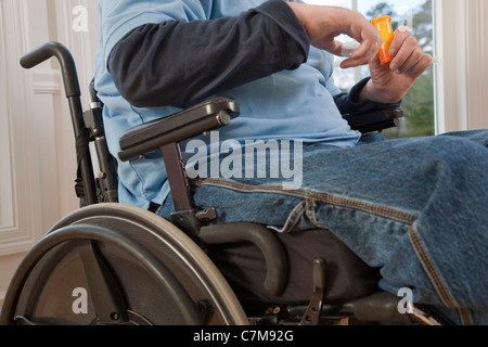 Man with spinal cord injury in a wheelchair taking pill from bottle with disabled hands Stock Photo