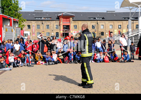 Fireman explaining fire hazards to school children on educational visit to National UK Rescue Organisations challenge event at Excel Centre London UK Stock Photo