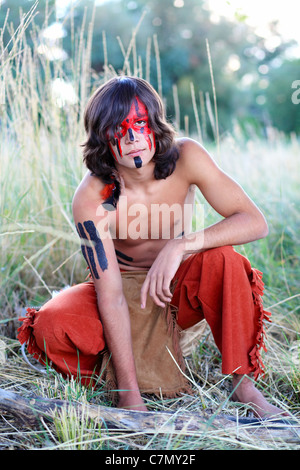 An American Indian boy squatting in tall grass Stock Photo