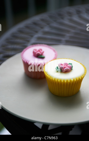 yellow and pink cup cakes on iron garden table upright yellow in foreground Stock Photo