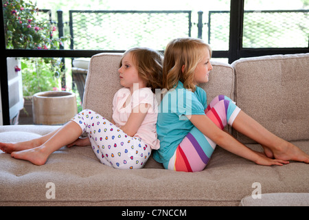 two girls sitting on the couch back to back Stock Photo
