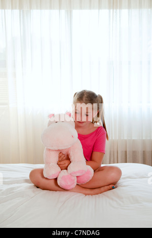 little girl sitting on bed playing with stuffed animal Stock Photo