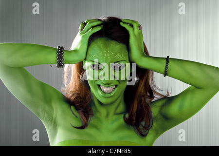 A green alien or Martian woman posing over a silver brushed metal backdrop. Stock Photo