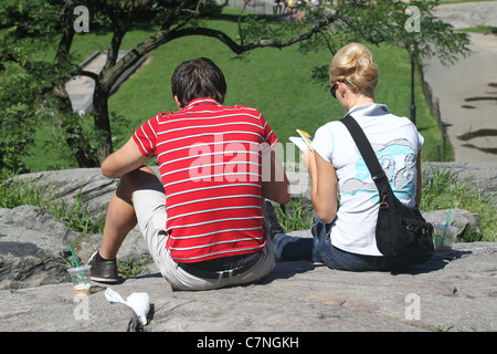 Two people sitting on a rock reading in a park Stock Photo