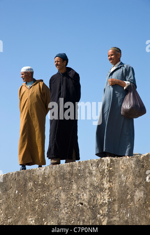 Three Moroccan gentlemen watching over the fishing boats from the harbour wall in Essaouira, Morocco Stock Photo