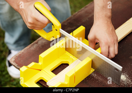 Man cutting a slat of wood using a saw and miter box outdoors. Stock Photo