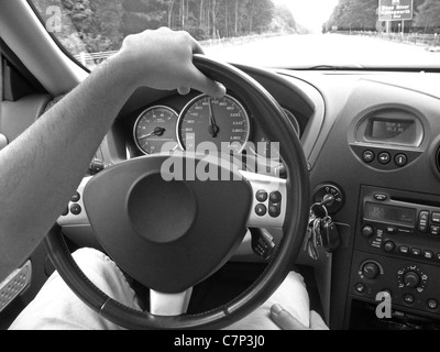 A man holds the steering wheel with one hand while driving on the highway. Stock Photo