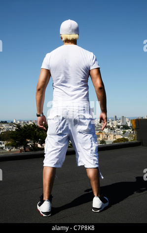 Back view of a trendy young man dressed in white standing on a roof. Stock Photo