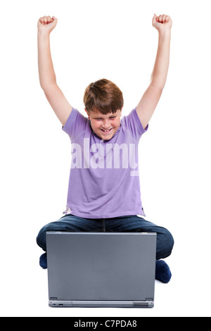 Photo of an 11 year old school boy sat with a laptop computer, his arms raised in the air, isolated on a white background. Stock Photo