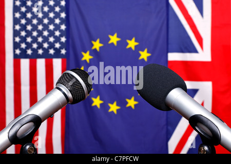 Two microphones on the stage of a press conference with the flags from America, European Union and the United Kingdom Stock Photo