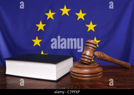 Still life photo of a gavel, block and law book on a judges bench with the European Union flag behind.
