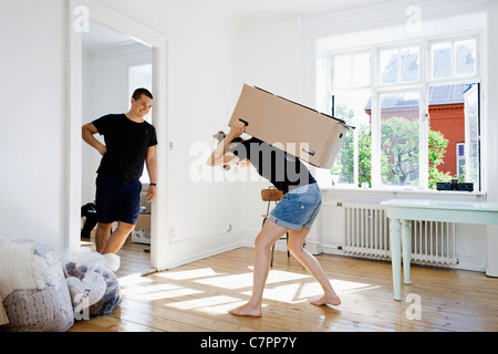 Man watching girlfriend carry heavy box Stock Photo