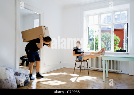 Woman watching boyfriend carry heavy box Stock Photo
