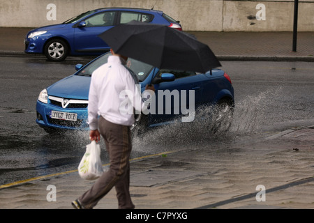 a car splashing through a puddle at the same time as a man carrying an umbrella passes Stock Photo