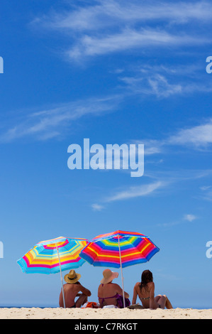 Family sitting on the beach sand under colourful umbrellas Stock Photo