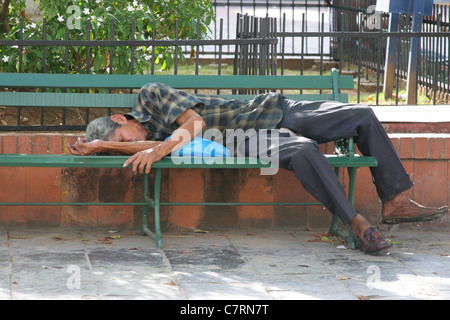 Homeless man sleeping in a park bench. Stock Photo