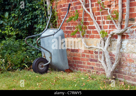 Wheelbarrow leaning against an old red brick wall in a country garden Stock Photo