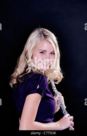 A beautiful blond blue eyed teenage girl flute player isolated against a black background in vertical format. Stock Photo